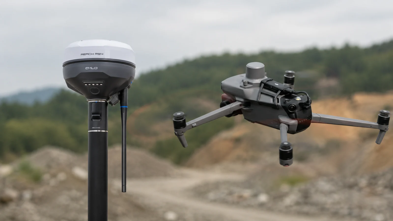 GPS-antenne op een meetstok naast een meetdrone in vlucht boven een grondstoffenterrein